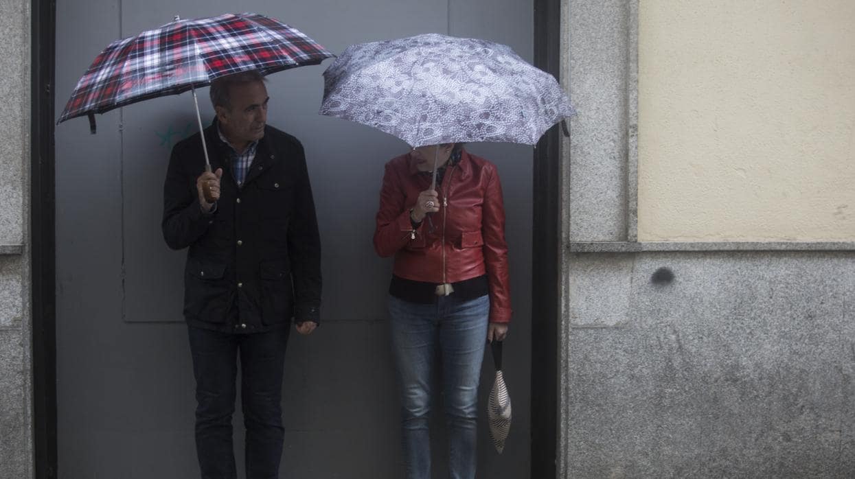 Dos sevillanos se resguardan de la lluvia bajo su paraguas