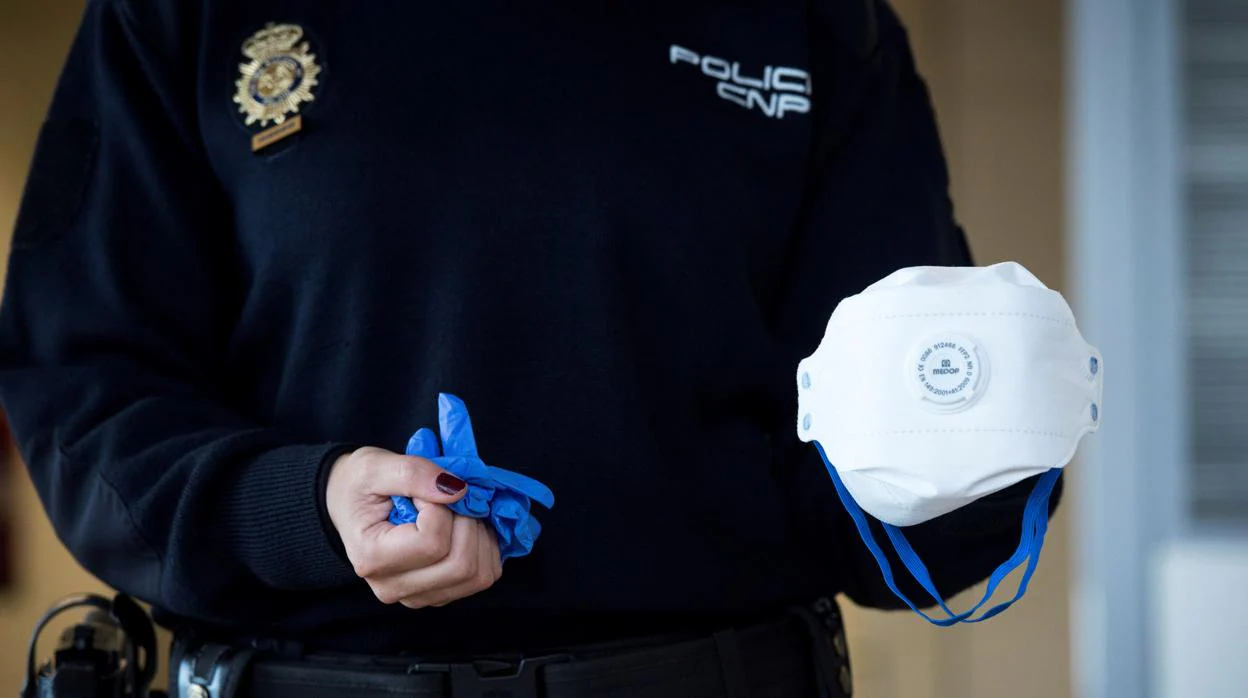 Un agente de la Policía Nacional muestra una mascarillas y unos guantes contra el coronavirus