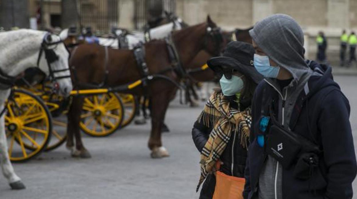 Dos turistas pasean por Sevilla con sus rostros cubiertos por mascarillas