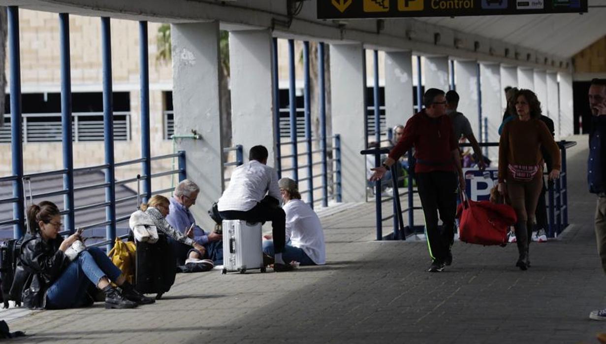 Pasajeros esperando en el exterior de la terminal, consultando sus teléfonos móviles.