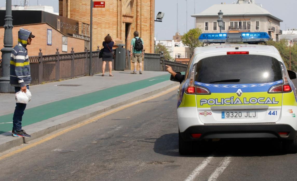 La Policía Local le hace una indicación a un joven; al fondo unos turistas haciendo fotos