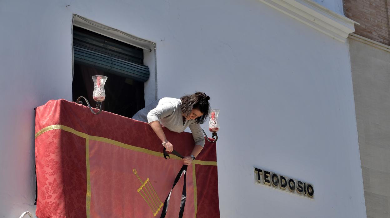 Una mujer coloca la colgadura de su balcón para el Domingo de Ramos en la calle Teodosio