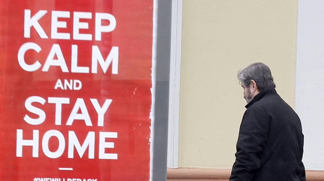 Un hombre camina junto a un cartel publicitario incitando a quedarse en casa