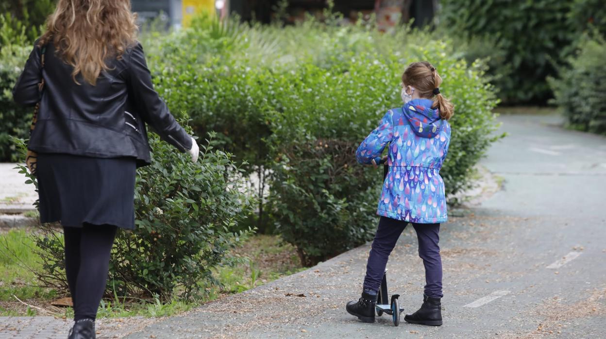 Una niña juega con su patinete bajo la supervisión de su madre