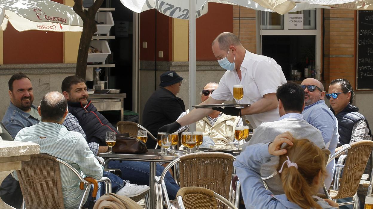 Un camarero sirve a los clientes de una mesa en la terraza de un bar en Sevilla