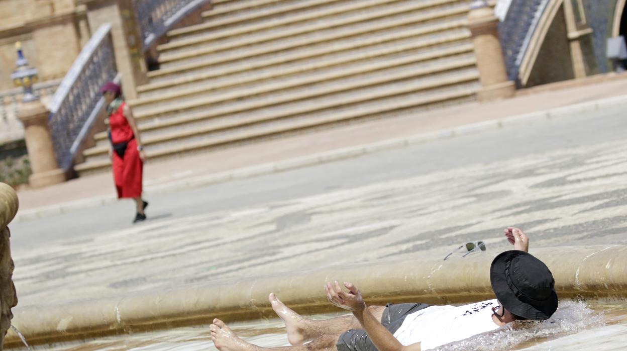 Un turista se refresca del calor en la fuente de la Plaza de España de Sevilla