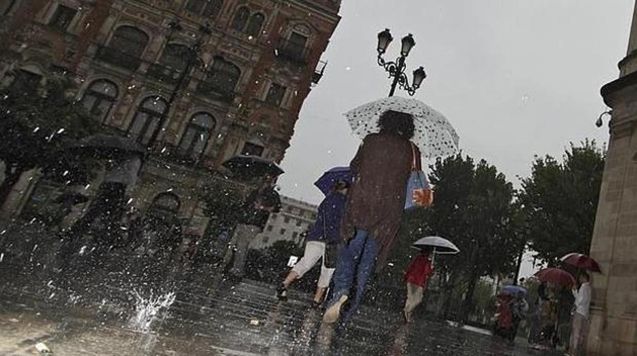 Varias personas pasean por Sevilla bajo la lluvia