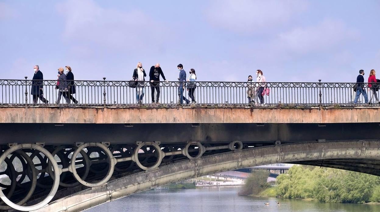 Varias personas pasean por el puente de Triana durante un día soleado en Sevilla