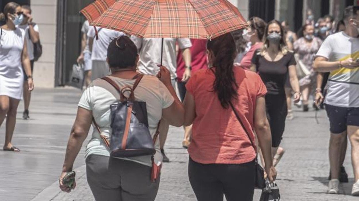 Dos jóvenes portan un paraguas para resguardarse del calor