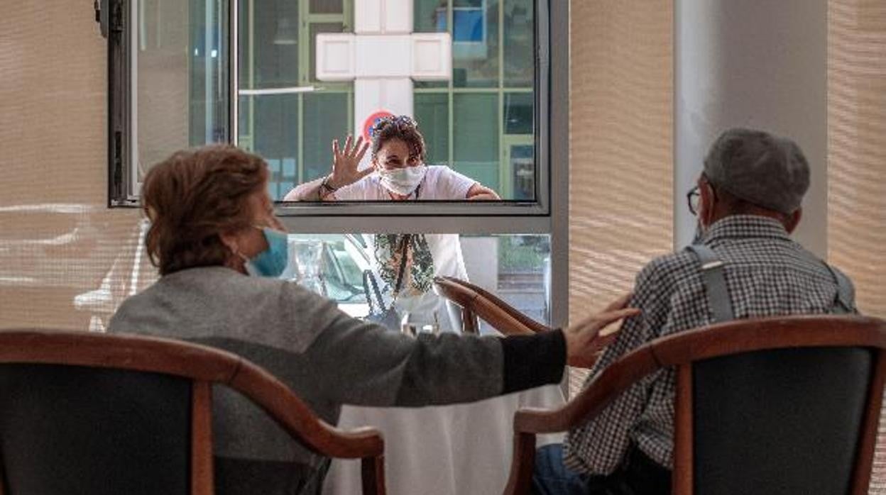 Una persona saluda desde una ventana a dos personas mayores de un geriátrico