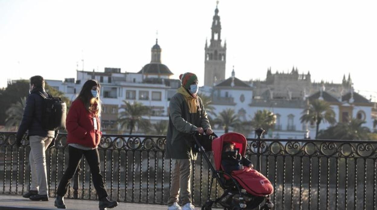 Varias personas pasean, protegidas con abrigos y ropa de invierno, por el puente de Triana de Sevilla