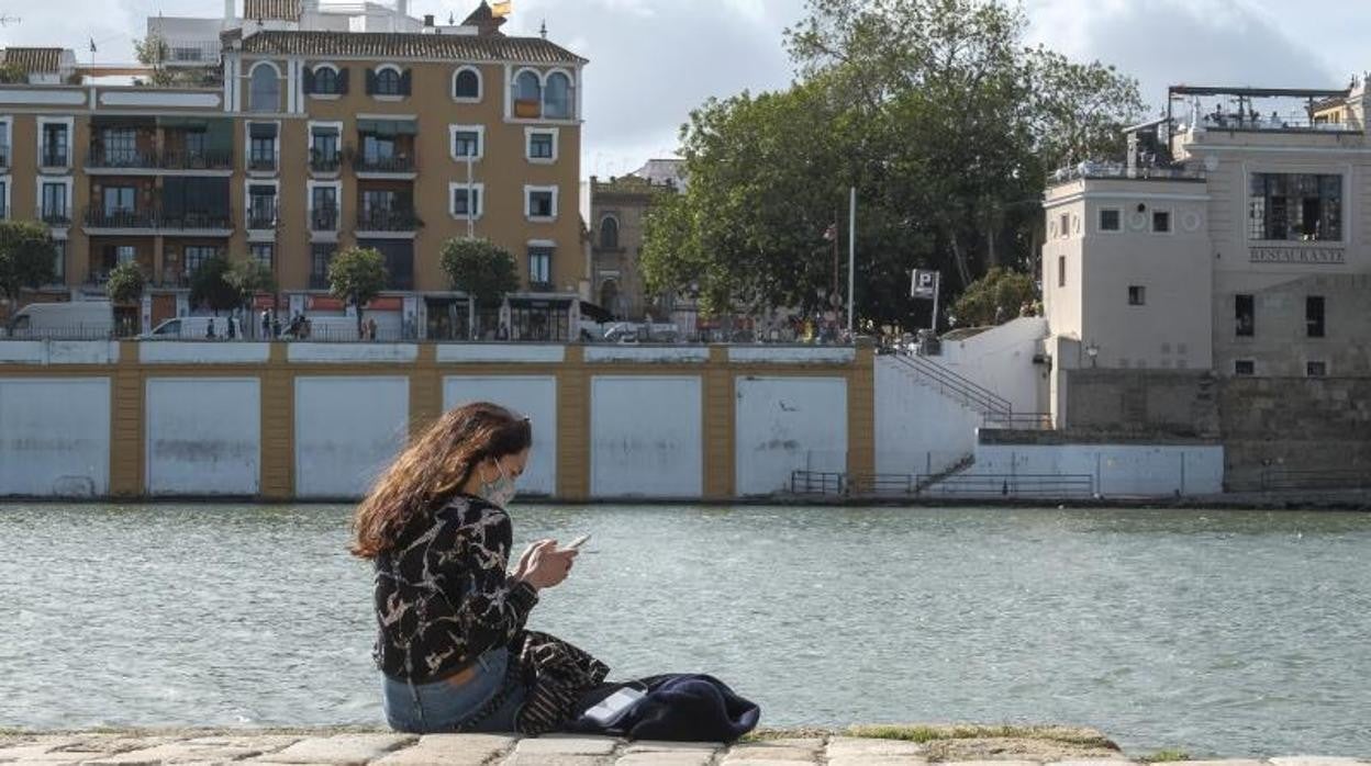 Una mujer mira el móvil en una de las orillas del río Guadalquivir en Sevilla