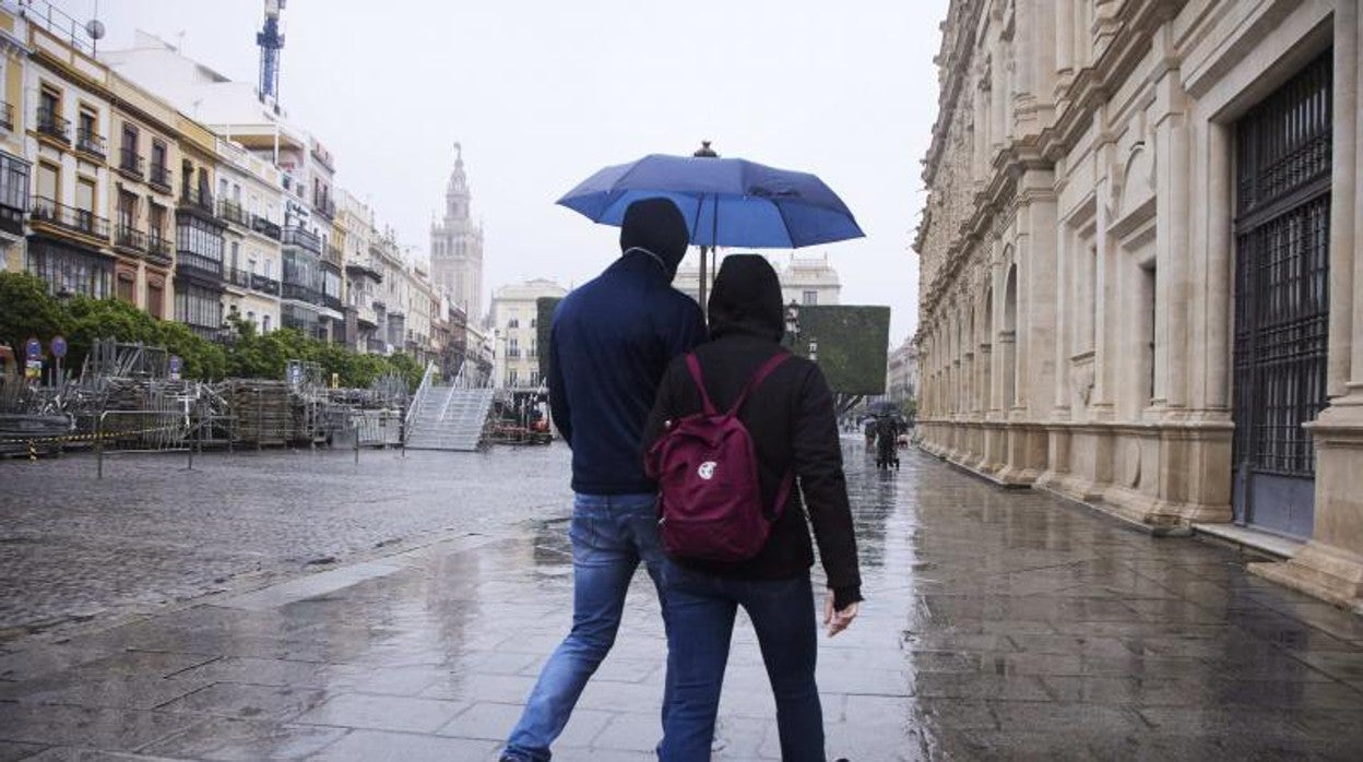 Dos personas se resguardan en un paraguas en la Plaza de San Francisco de Sevilla