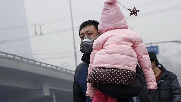 Un hombra camina por las calles de Pekín con su hija en brazos y protegido con una mascarilla