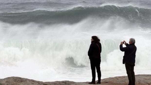 Dos personas observan las olas esta tarde en Muxía, A Coruña. La Xunta de Galicia ha decretado alerta roja ante la previsión de fuertes olas en litoral de La Coruña y Lugo que podrían alcanzar los nueve metros