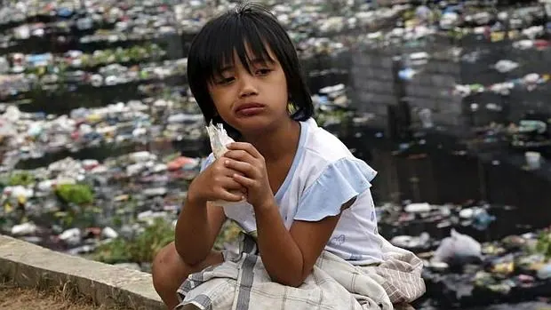 Una niña toma un tentempié junto a un río plagado de basura en Manila (Filipinas)