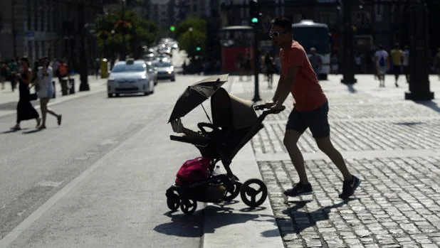 Días de altas temperaturas en Madrid: en la imagen, un padre con su bebé muy protegido cruzan la Puerta del Sol