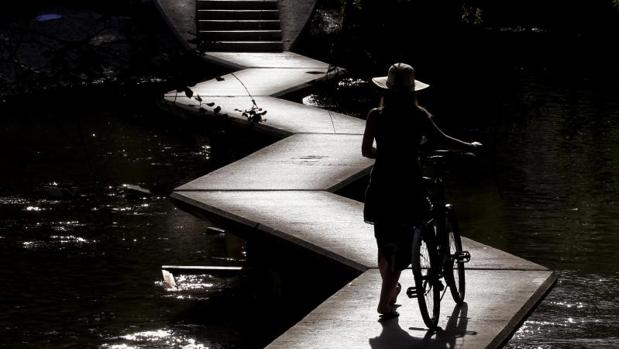 Una mujer pasea con su bicicleta a las orillas del río Arga a su paso por Pamplona