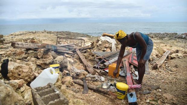 Una mujer se prepara la comida junto a los restos de lo que fue su casa tras el paso del huracán Matthew por Haití