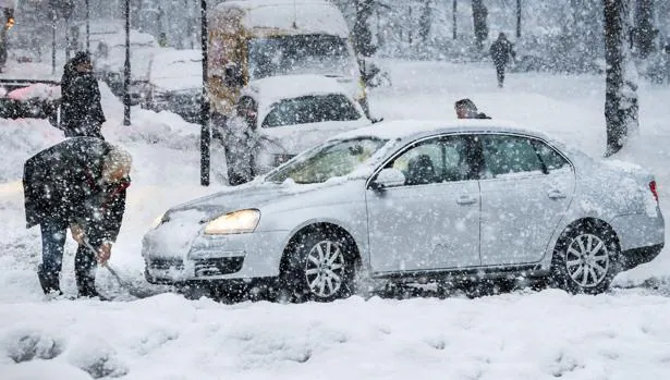 Un hombre limpia la calle de nieve para tratar de sacar su coche durante una nevada en Estocolmo