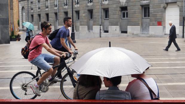 Varias personas se protegen de la lluvia esta tarde en la calle Pelayo, en el centro de Oviedo