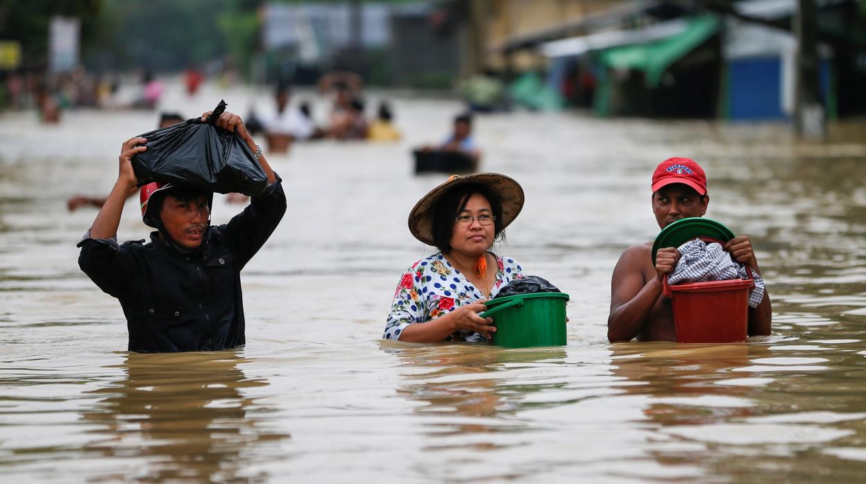 Varias vecinos cargan con sus pertenencias mientras atraviesan una calle inundada por las lluvias monzónicas en la región de Bago