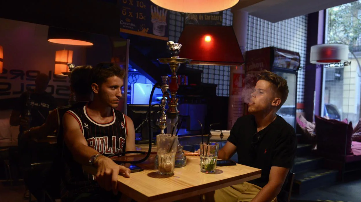 Dos jóvenes fuman cachimba en un establecimiento