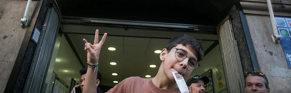Cosmin, con el billete premiado, frente a la administración de lotería de Barcelona donde dice que él compró el décimo