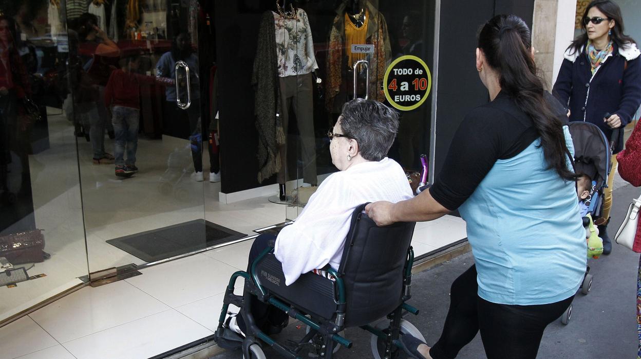 Una mujer empujando la silla de ruedas de una persona con discapacidad