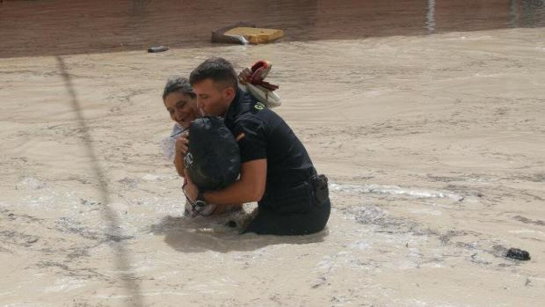 Un policia ayuda a una vecina de Almoradí tras inundarse las calles de la población por la rotura del dique del cauce del río Segura tras el paso de la Gota Fría