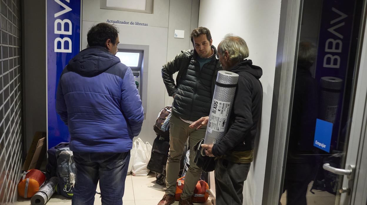 Un voluntario reparte kits de abrigo a dos personas sin hogar que duermen en un cajero