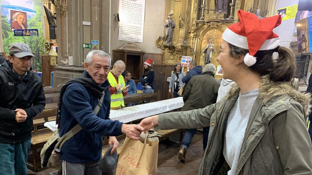 Una joven del Ateneo Universitario entrega una bolsa de comida a un hombre en la parroquia de San Antón