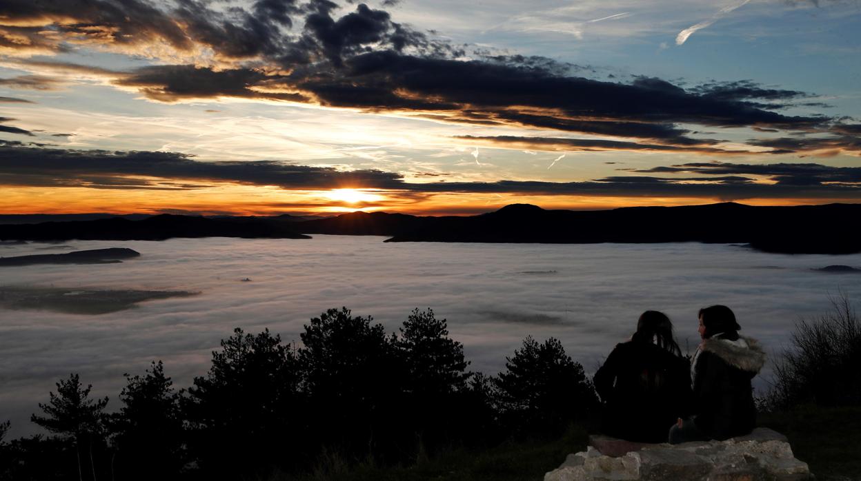 Dos personas observan desde el alto de san Cristóbal el atardecer a pesar de la niebla