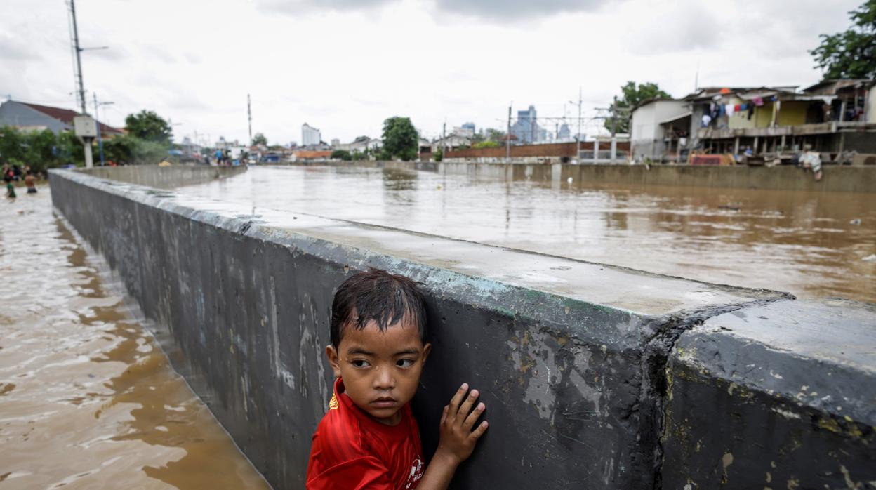 Un niño se protege tras un muro en una carretera inundada de Yakarta