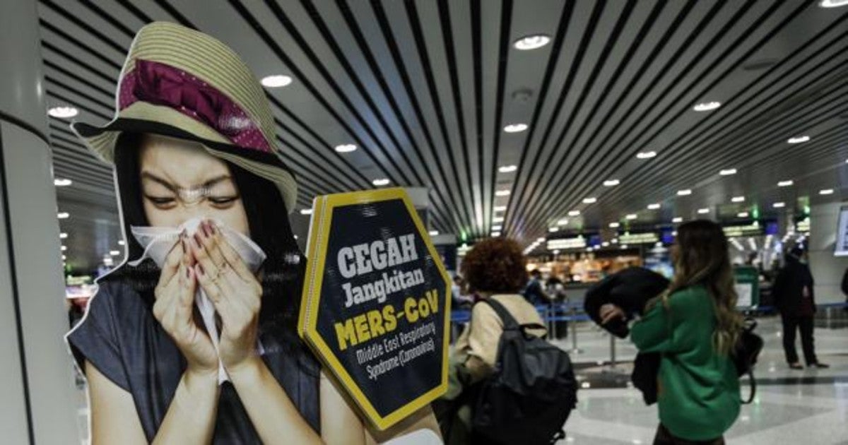 Pasajeros en el aeropuerto de Kuala Lumpur junto a un cartel que alerta del riesgo del nuevo coronavirus