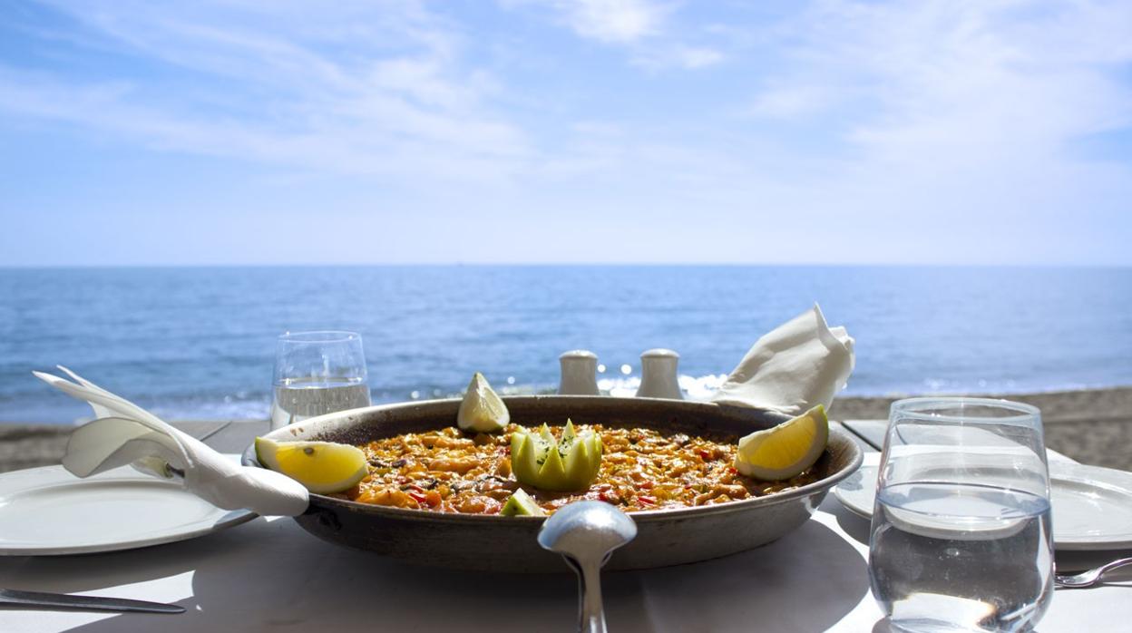 Fotografía de archivo de una mesa de comensales con una paella y vistas al mar