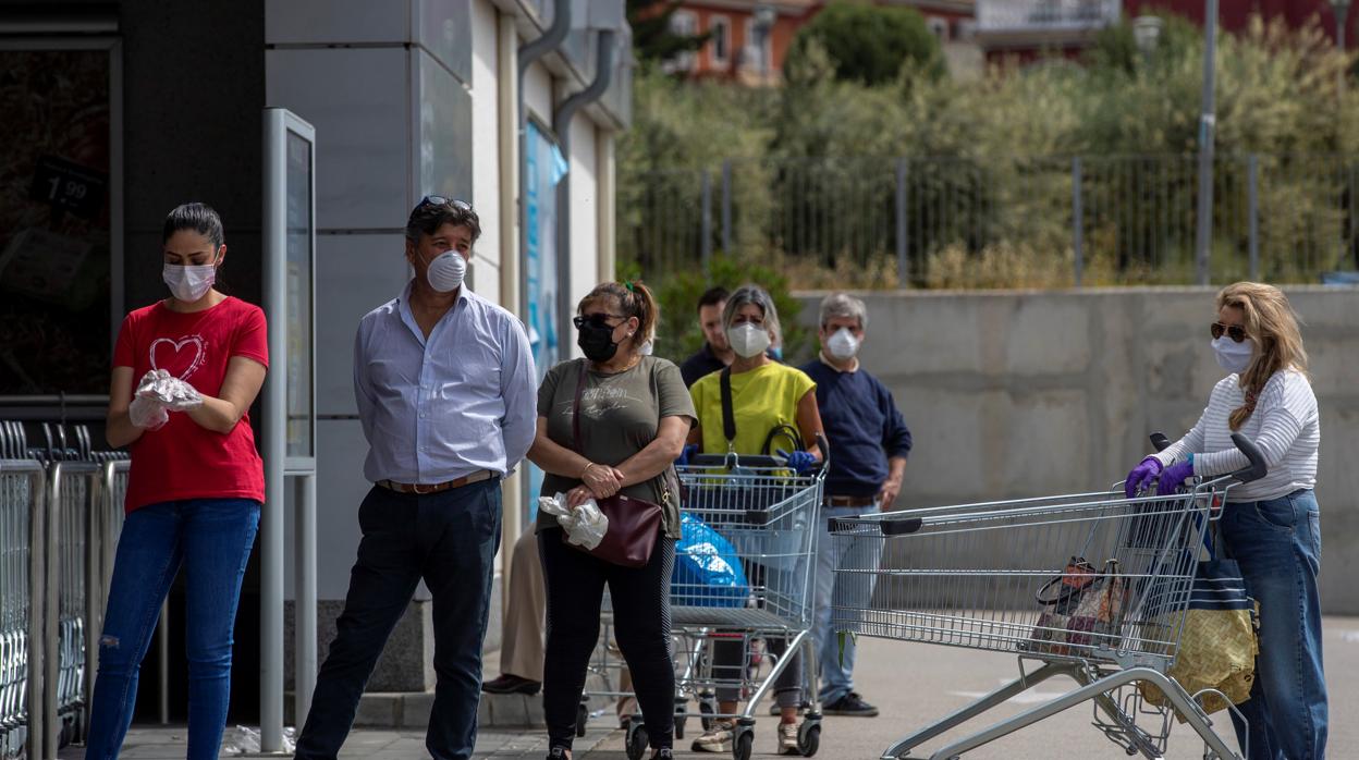 Varias personas protegidas con mascarillas hacen cola hoy en la entrada de un supermercado en Gines (Sevilla)