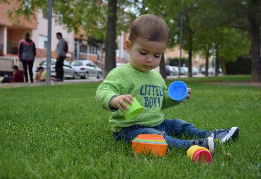 Sergio juega en el césped en primer plano y detrás, dos madres con sus hijos