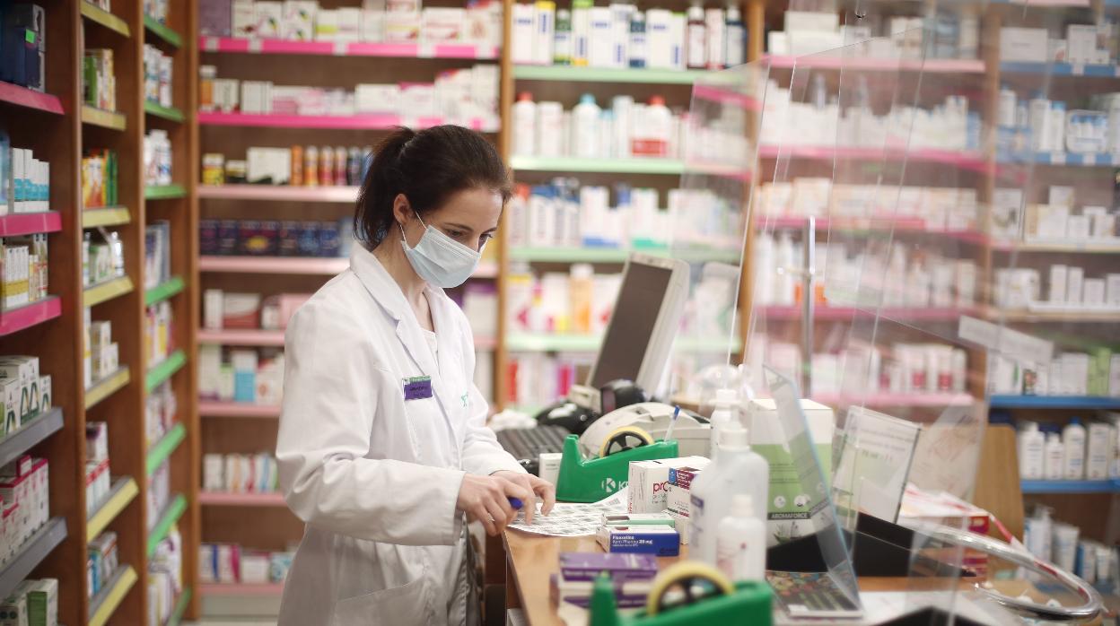 Una farmacéutica con mascarilla despacha en una farmacia de Madrid