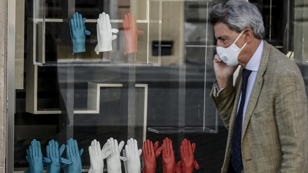 Un hombre con mascarilla pasa por delante de un escaparate con guantes que forman la bandera tricolor