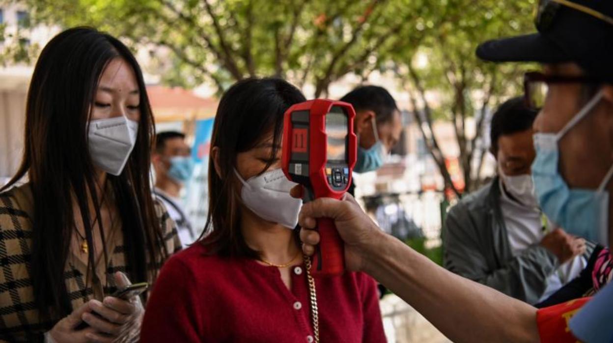 Un trabajador comprueba la temperatura corporal de los pasajeros antes de que tomen un taxi después de llegar a la estación de tren de Hankou en Wuhan