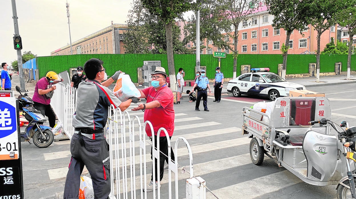 Los repartidores a domicilio traen hasta la barrera policial comida para los vecinos confinados alrededor del mercado de Xinfadi, que los voluntarios les llevan hasta sus casas
