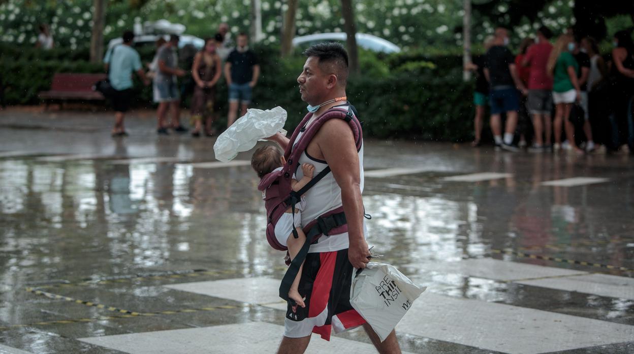 Un hombre protege a un bebé de la lluvia a las puertas de la Ciudad de la Justicia de Valencia