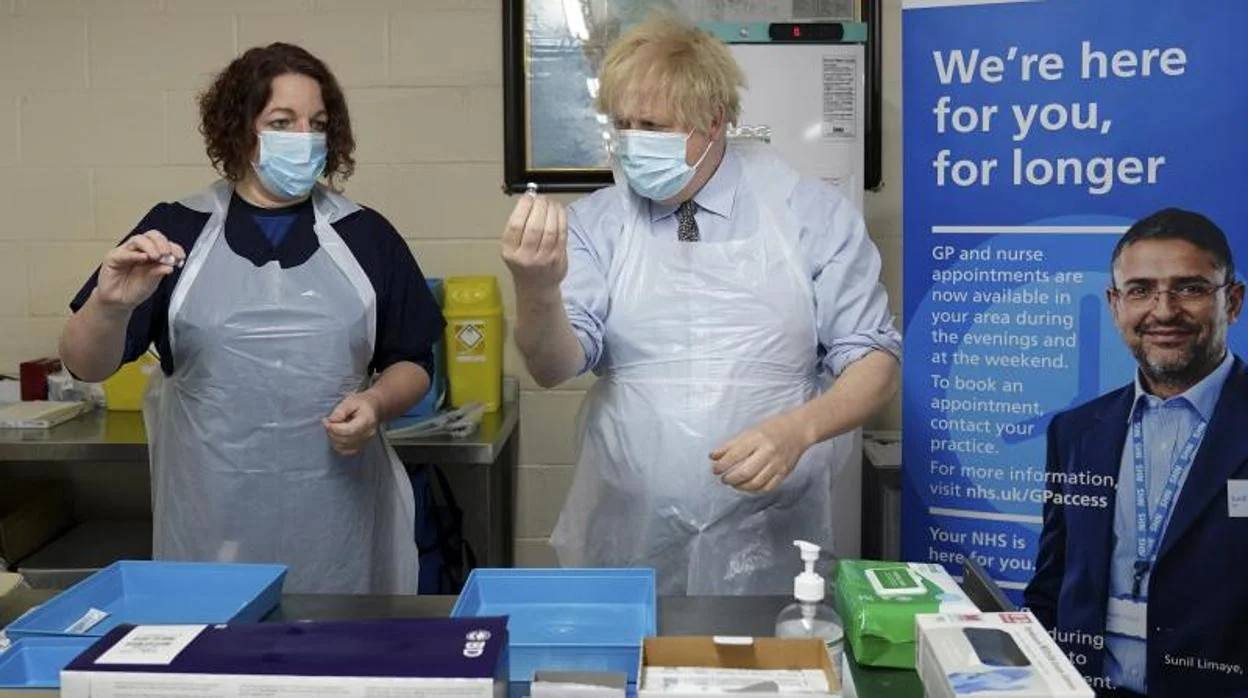 Boris Johnson sostiene un vial de la vacuna junto a una sanitaria