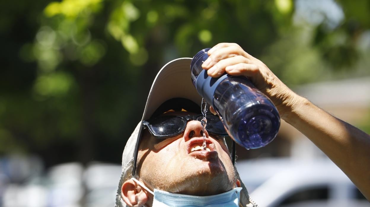 Un hombre bebe agua con la mascarilla retirada