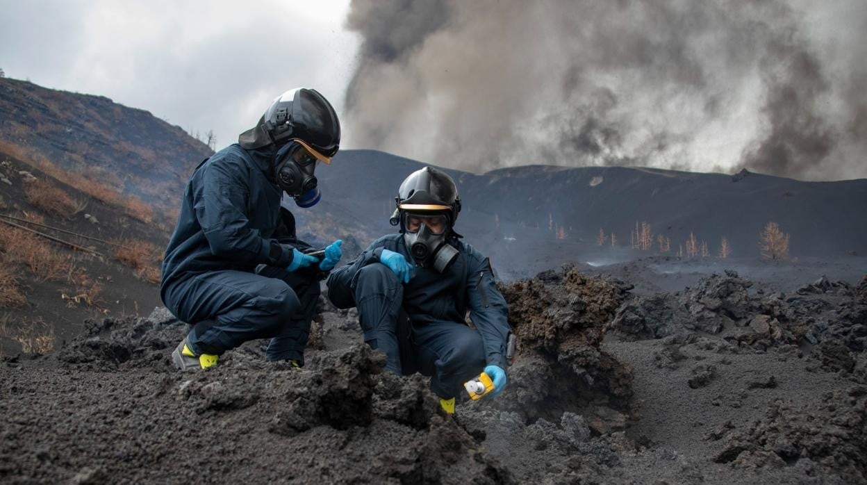 Dos militares de la UME miden la toxicidad de los gases en la lava, cerca de Cumbre Vieja, con las fumarolas del volcán en el horizonte cercano