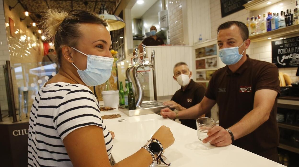 Una mujer con la mascarilla puesta pide su consumición en un bar de Sevilla