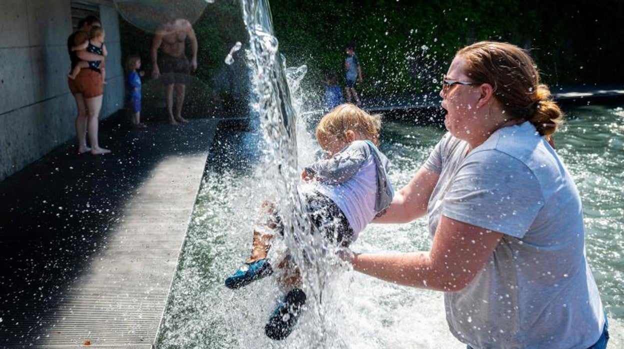 Una mujer sostiene a un niño pequeño bajo una cascada en un parque en Washington DC, el 28 de junio de 2021, durante la ola de calor en Estados Unidos