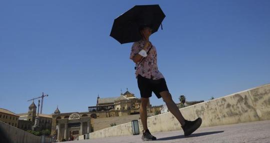 Un hombre pasea por Córdoba protegido por un paraguas contra el calor