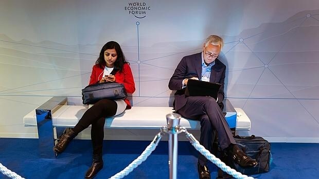 Dos participantes del Foro Económico Mundial consultan sus dispositivos